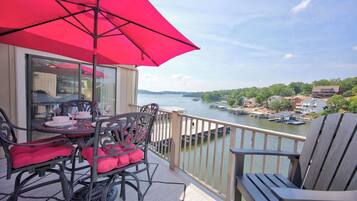 A balcony with a table and chairs, a red umbrella, and a view of a river with boats.