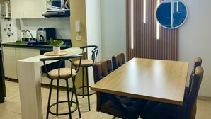 Une cuisine compacte dotée d’appareils électroménagers modernes, un coin repas avec une table et des chaises en bois, et un panneau décoratif mural.