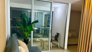 Un salon moderne avec un canapé gris, une grande plante en pot et une porte-fenêtre coulissante donnant sur un coin repas.