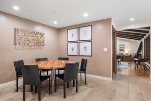 Un comedor con una mesa redonda de madera y sillas negras, una obra de arte en la pared e impresiones botánicas enmarcadas.