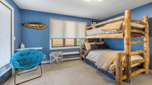 Una habitación con literas, una silla, un ventanal y un ventilador.