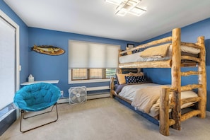 Ein Zimmer mit einem Etagenbett, einem Stuhl, einem Fenster und einem Ventilator.
