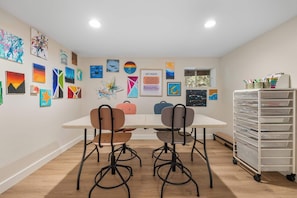 Ein Atelier mit einem weißen Tisch, zwei Stühlen und einer Wand voller verschiedener Kunstwerke.