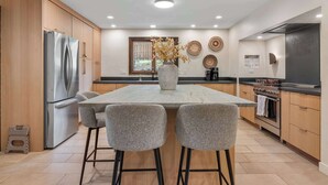 Una cocina moderna con una isla central, taburetes de bar, un refrigerador, un horno y placas decorativas en la pared.