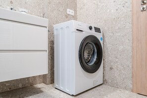 A compact, modern laundry room with a front-loading washing machine, a white cabinet, and a marble-tiled wall. - Blueground | Nusle, balcony & equipped, nr cafes (PRG-75) (Prague)