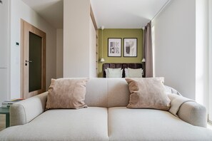 A modern hotel room with a sofa bed, a green accent wall, and a visible bed in the background. - Blueground | Nusle, balcony & equipped, nr cafes (PRG-75) (Prague)