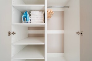 A white closet with shelves, a hanging rod, and a metal door. - Blueground | Nusle, balcony & equipped, nr cafes (PRG-75) (Prague)