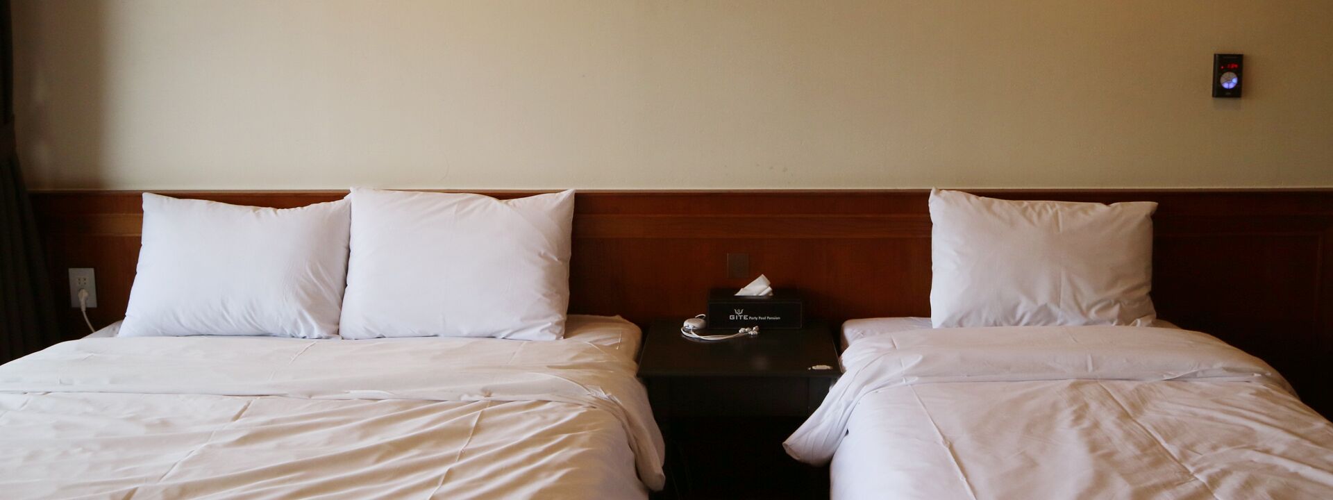 Habitación de hotel con dos camas, una mesita de noche con una caja de pañuelos y un reloj de pared.