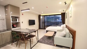 A hotel room with a bed, a sofa, a dining table with chairs, a TV, and a kitchen area with a microwave. - GITE Hotel Yeosu (Yeosu)