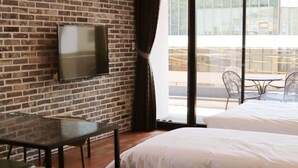 A hotel room with a brick wall, a flat-screen TV, a small table, two beds, and a balcony with outdoor seating. - GITE Hotel Yeosu (Yeosu)