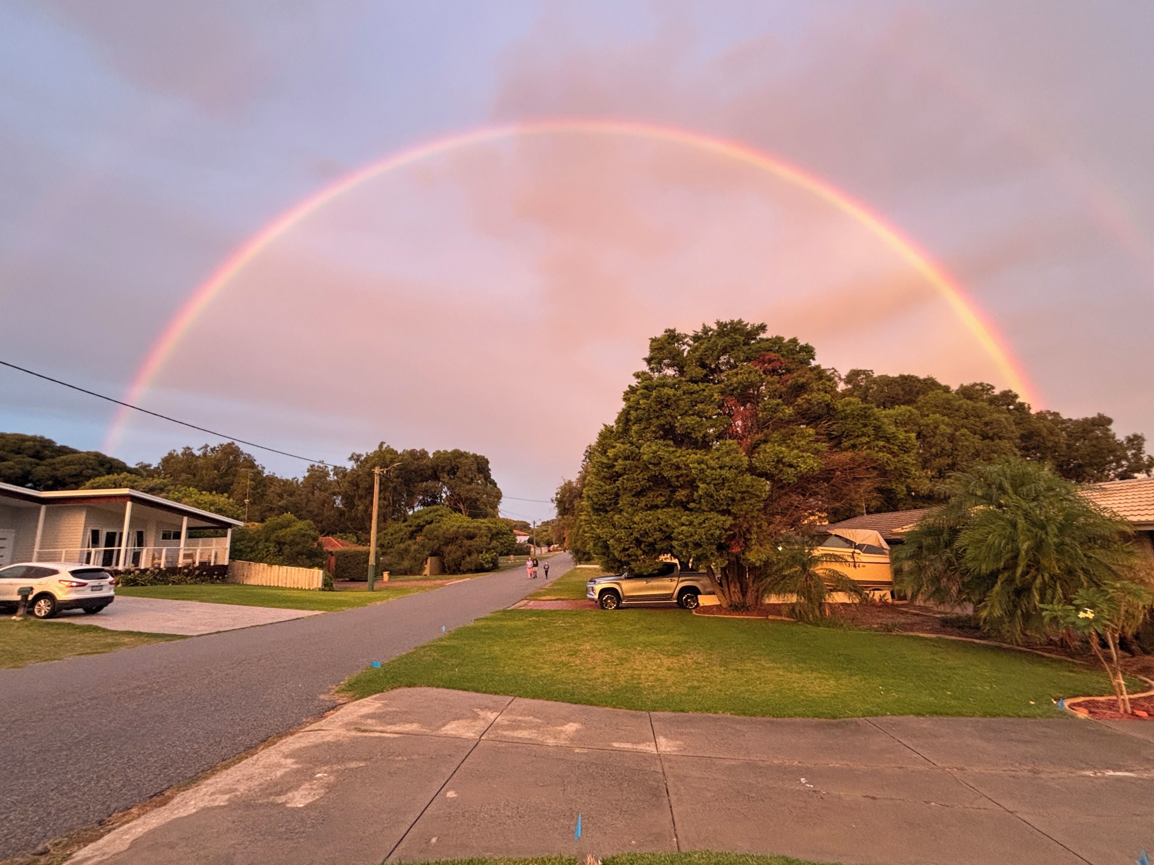 A residential street with houses, a tree, and a rainbow.