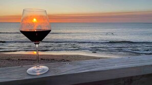 Um copo de vinho tinto sobre uma superfície de madeira, vista para o oceano e um pôr do sol.