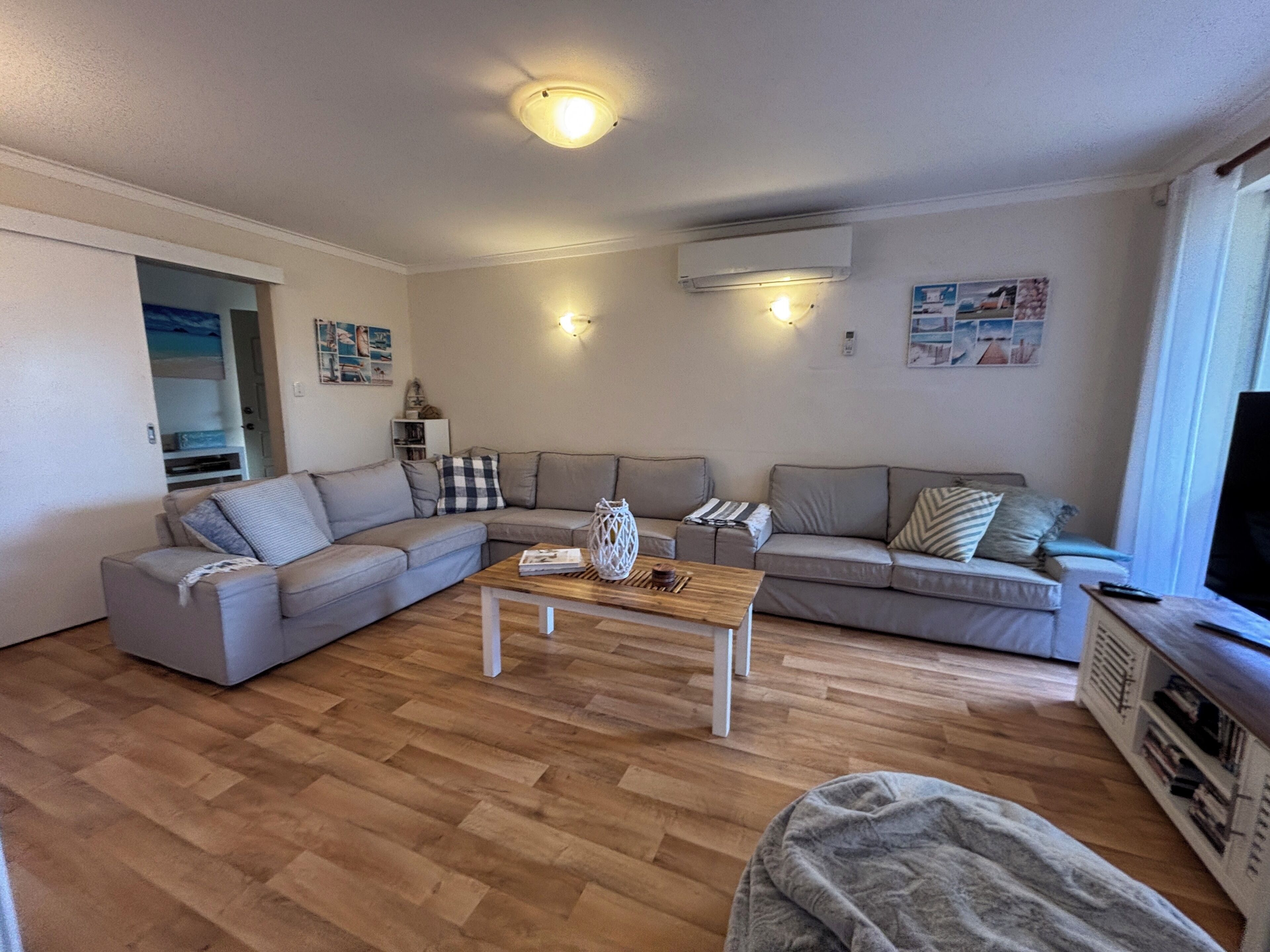 A living room with a sectional sofa, a coffee table, a TV stand, and a ceiling light.