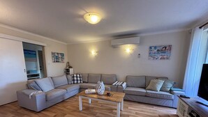 Ein Wohnzimmer mit Ecksofa, Couchtisch, TV-Schrank und Deckenleuchte.