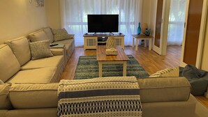 Ein Wohnzimmer mit einer Couch, einem Couchtisch, einem Fernseher und einem Fenster mit Vorhängen.