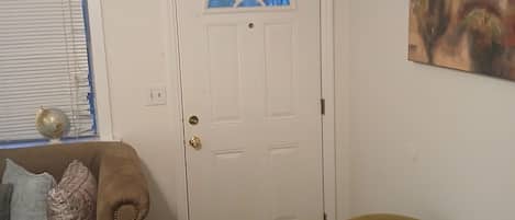 A room with a brown leather couch, a white door with a blue glass window, and a painting on the wall.