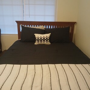 Un lit avec une tête de lit sombre, un coussin à motifs et une couvre-lit à rayures.