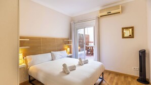 Ein Hotelzimmer mit Bett, Nachttisch, Lampe, Klimaanlage und Blick ins Freie.