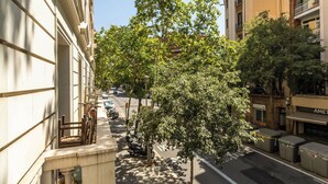 Eine von Bäumen gesäumte Straße mit Gebäuden an beiden Seiten, blauem Himmel und geparkten Fahrzeugen.