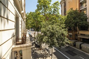 Eine von Bäumen gesäumte Straße mit Gebäuden an beiden Seiten, blauem Himmel und geparkten Fahrzeugen.