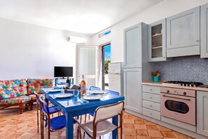 A modern kitchen with a dining area, featuring a blue table set for two, a sofa with a colorful floral pattern, and a large window. - Casa Spiaggiabella - Coastal Home Near The Sea, Lecce (Spiaggiabella), Italy (Lecce (Spiaggiabella))