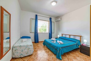 Een slaapkamer met twee bedden, een raam met gordijnen, een spiegel en een nachtkastje met een lamp.