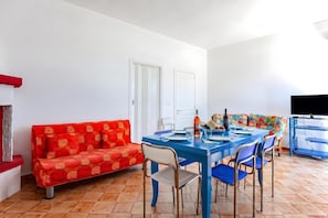 A dining area with a blue table, red patterned sofa, and a television on a stand. - Casa Spiaggiabella - Coastal Home Near The Sea, Lecce (Spiaggiabella), Italy (Lecce (Spiaggiabella))