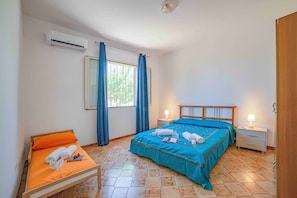 A bedroom with a bed, a bedside table, a nightstand, an air conditioning unit, and a window with curtains.