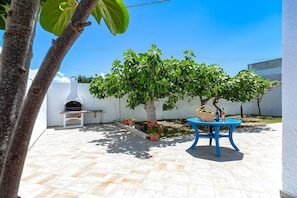 A patio area with a white wall, a small table, a blue table, potted plants, and a tree. - Casa Spiaggiabella Near The Sea, Lecce (Spiaggiabella), Italy (Lecce (Spiaggiabella))