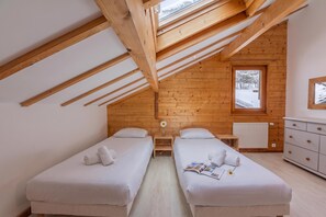 A room with two beds, wooden beams, a window with a view of snow-covered trees, a radiator, and a dresser. - Chalet Skyline Mont Blanc, Servoz (Chamonix), France (Servoz (Chamonix))
