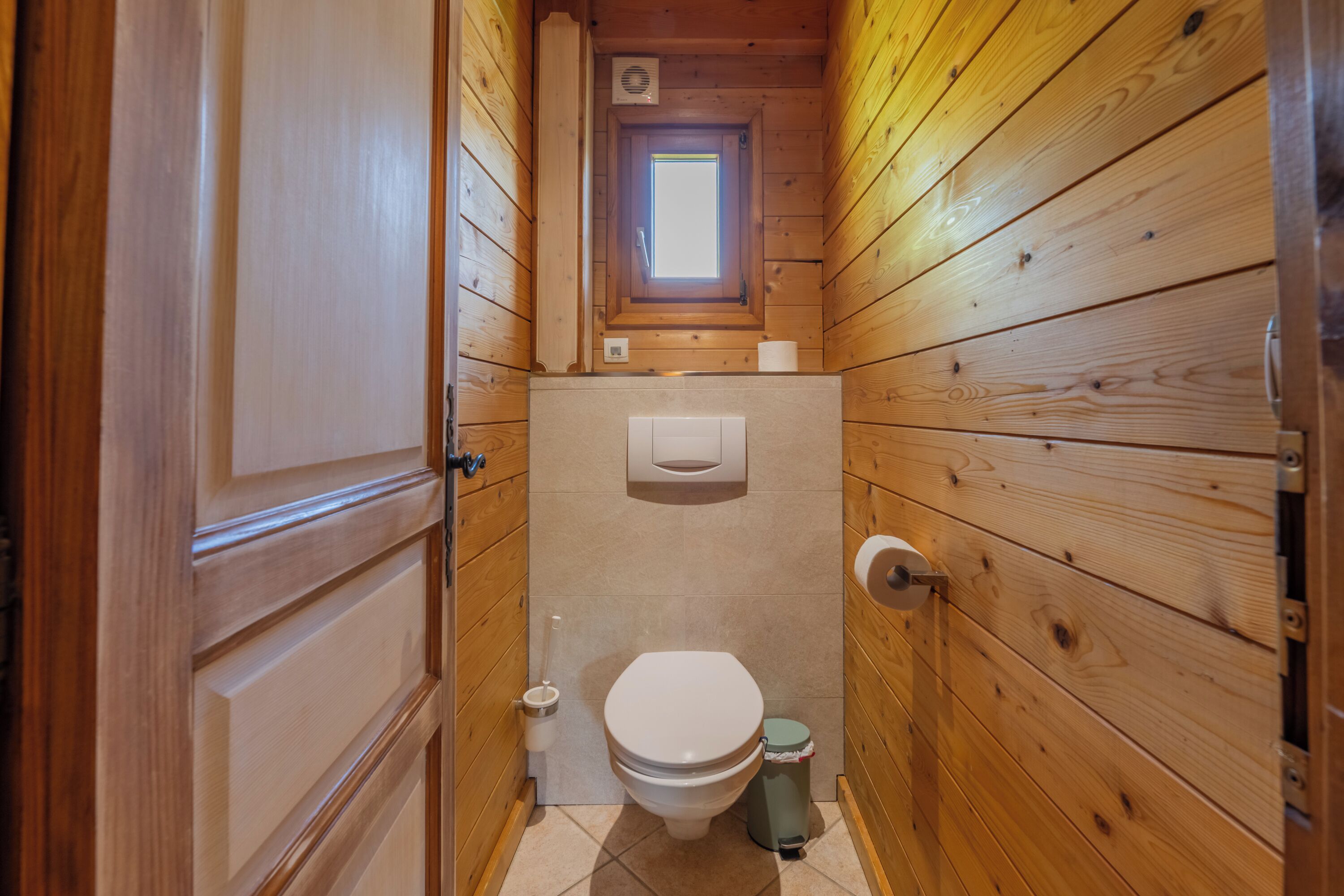 A wooden-paneled bathroom with a toilet, a window, and a small skylight.