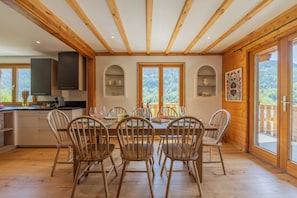 Ein Essbereich mit Holzbänken und einem Tisch, Holzbalken an der Decke und großen Fenstern mit Blick auf Grünflächen.