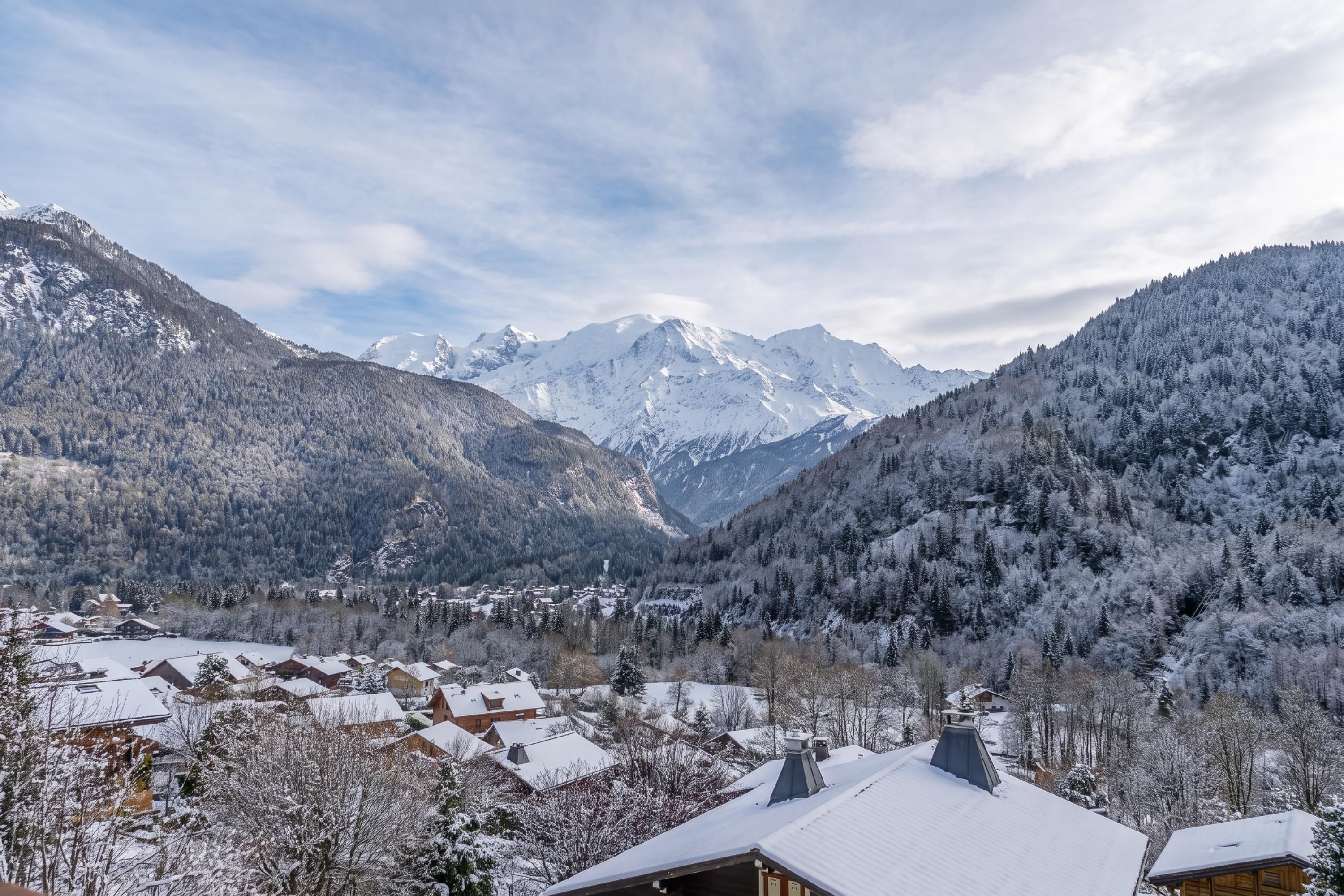 A mountainous landscape with snow-covered peaks and a valley with buildings.