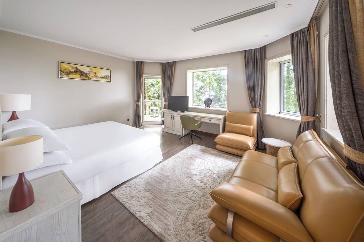 Habitación de hotel con cama, escritorio, silla, sofá y ventana con cortinas.