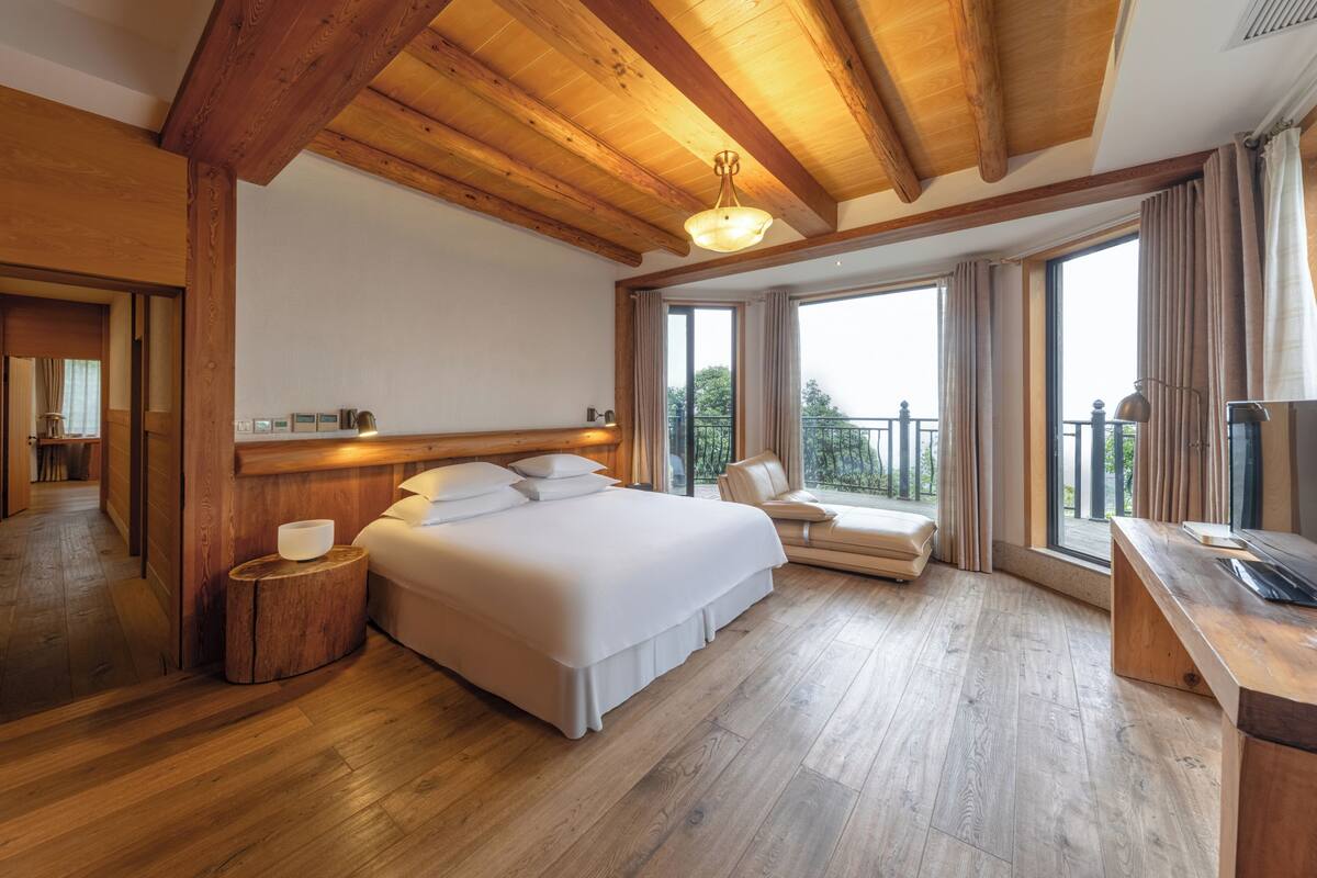 Un dormitorio amplio con una cama grande, techo de madera y un balcón con vistas.