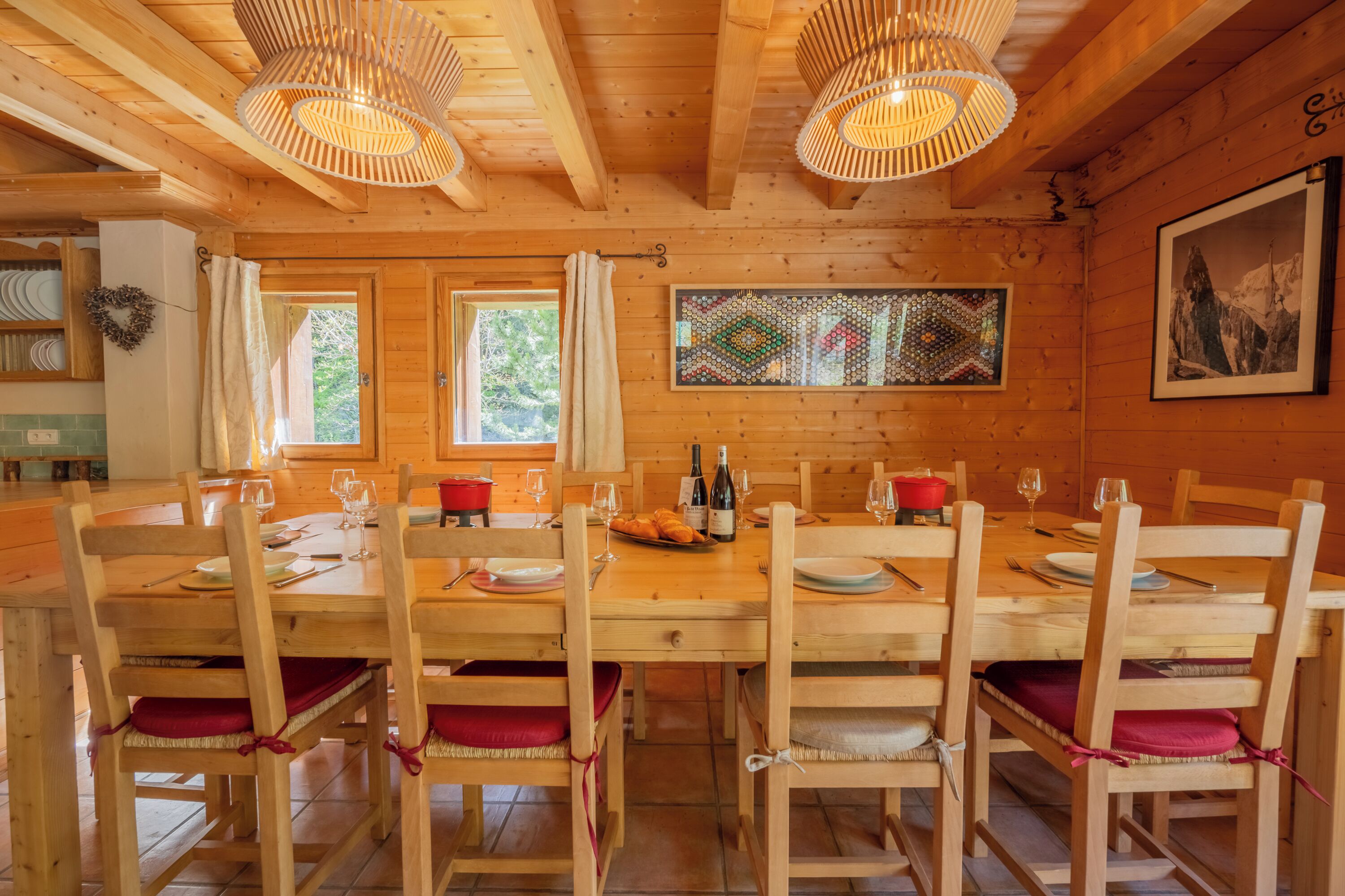 A wooden dining room with a large table set for six, surrounded by chairs with red cushions.