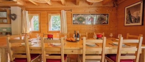 Une salle à manger en bois avec une grande table dressée pour six personnes, entourée de chaises dotées de coussins rouges.
