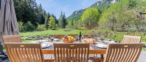 Une terrasse en bois avec une table dressée pour six personnes, entourée de chaises, offrant une vue sur un paysage montagneux.