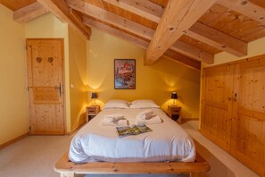 A bedroom with a wooden ceiling, a bed with white linens, two bedside tables with lamps, and a door with heart-shaped cutouts. - Chalet Montet Forest River Garden Lodge, Vallorcine (Argentiere), France (Vallorcine (Argentiere))