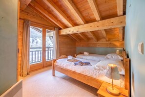 Ein Schlafzimmer in einer Holzhütte mit einem Bett, einem Nachttisch, einer Lampe und Blick auf eine verschneite Landschaft durch ein Fenster.
