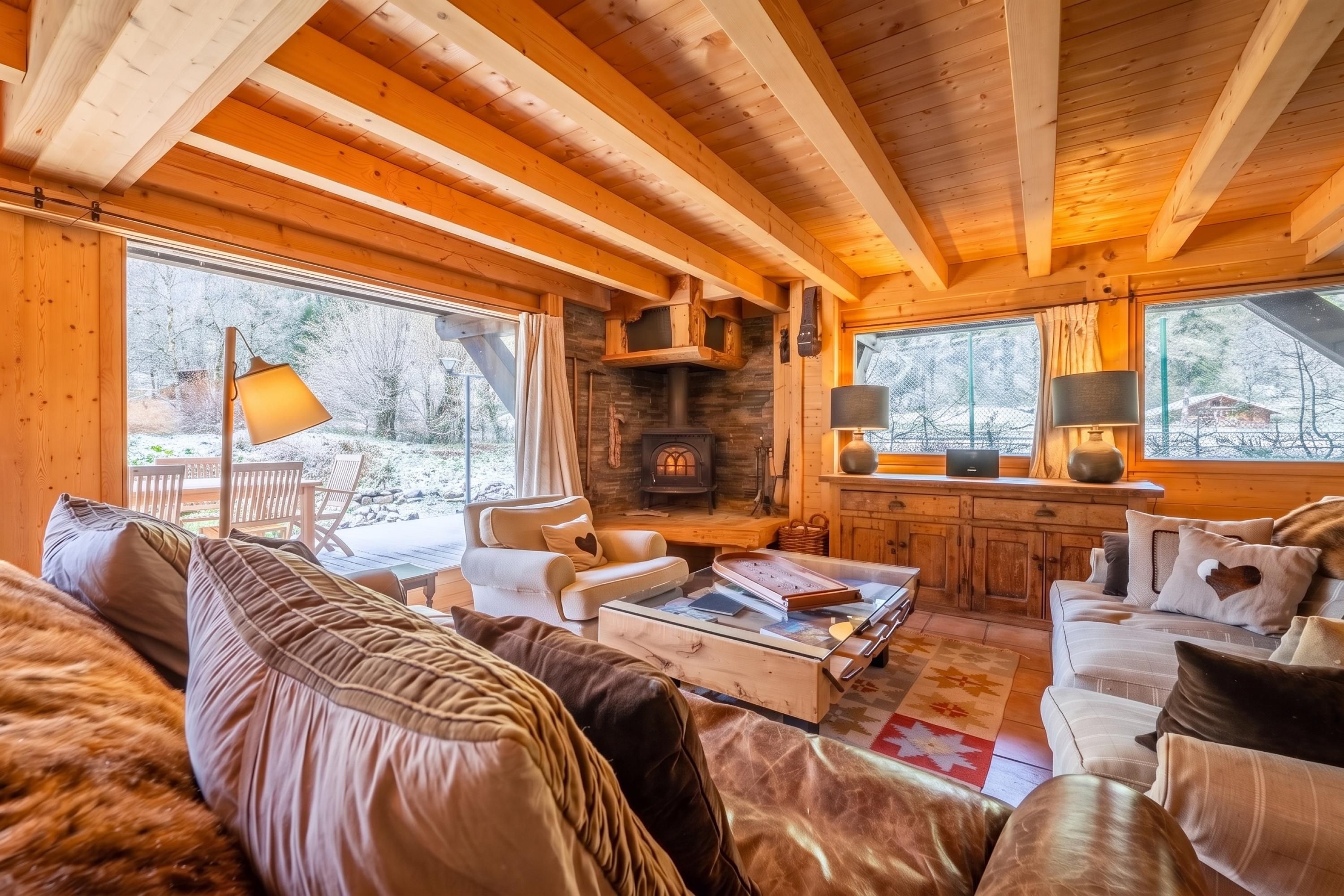 A cozy log cabin interior with a fireplace, wooden furniture, and large windows.