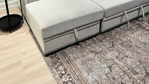 Un salon moderne avec un canapé d’angle, un tapis à motifs, une petite table d’appoint et un lampadaire.