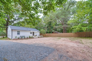 A single-story house with a gravel driveway, a wooden fence, and a tree-lined yard.