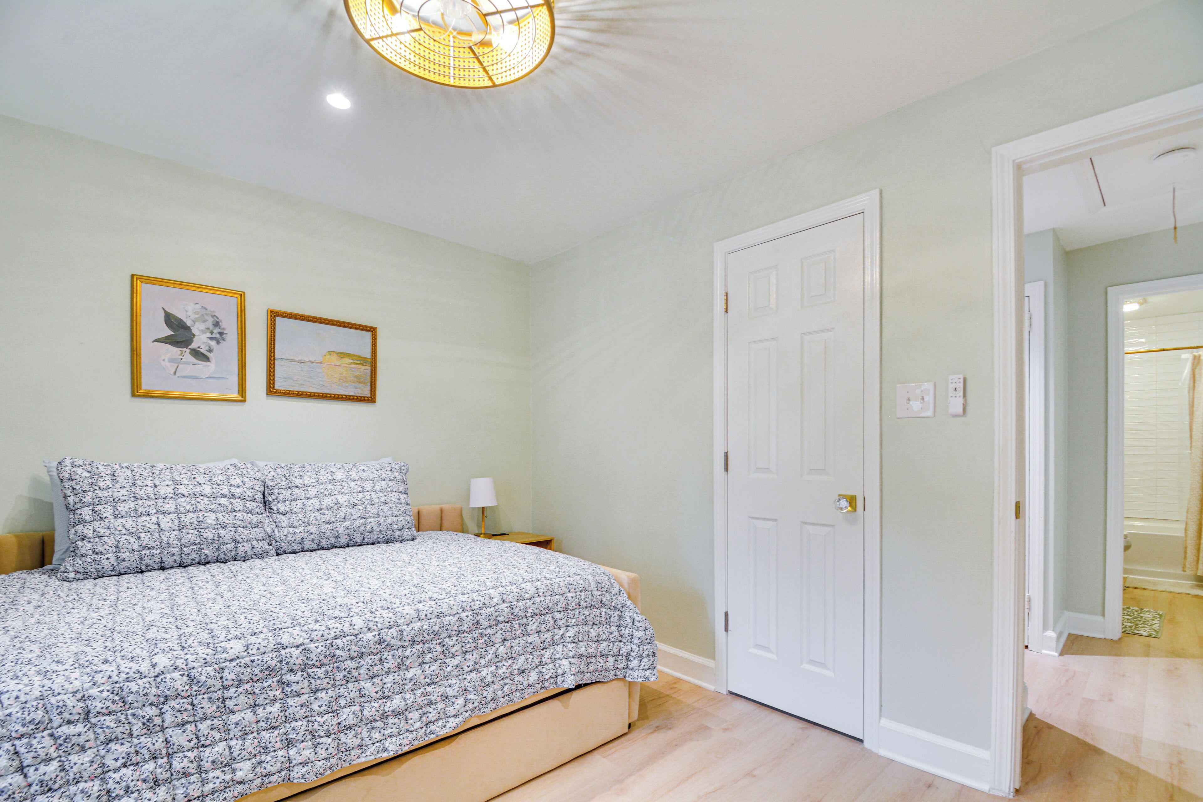 Un dormitorio con una cama, dos cuadros en la pared, una puerta y una lámpara.