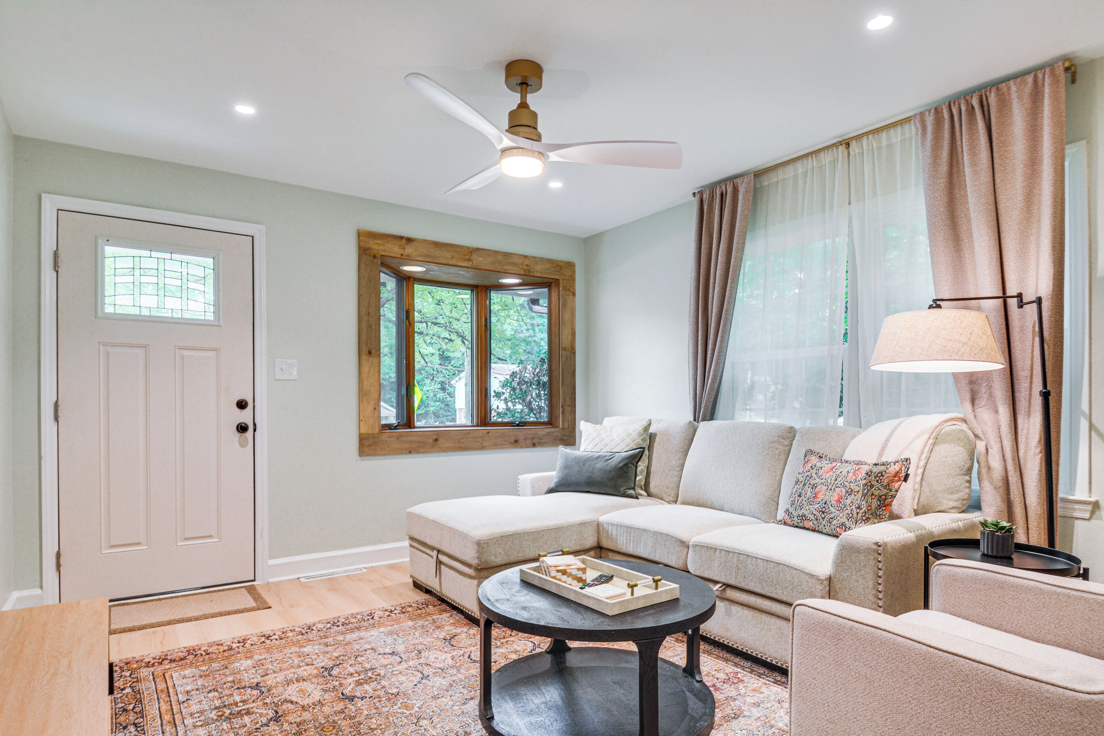 A living room with a sectional sofa, a coffee table, a ceiling fan, a window with curtains, and a door with a window.