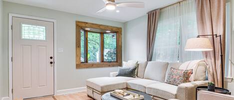 A living room with a sectional sofa, a coffee table, a ceiling fan, a window with curtains, and a door with a window.
