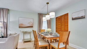 Un coin repas avec une table dressée pour six personnes, des chaises en bois, un lustre et un tableau accroché au mur.