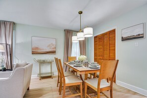 Comedor con una mesa dispuesta para seis personas, sillas de madera, una araña y un cuadro en la pared.