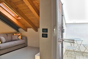 Ein Zimmer mit Holzbalkendecke, einer Couch, einem kleinen Tisch und einer Schiebetür zu einem Außenbereich mit Tisch und Stühlen.
