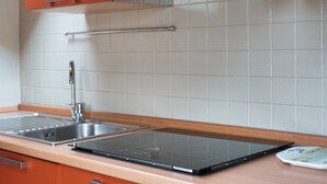 Ett modernt kök med en diskho i rostfritt stål, en svart induktionshäll och orange köksinredning.